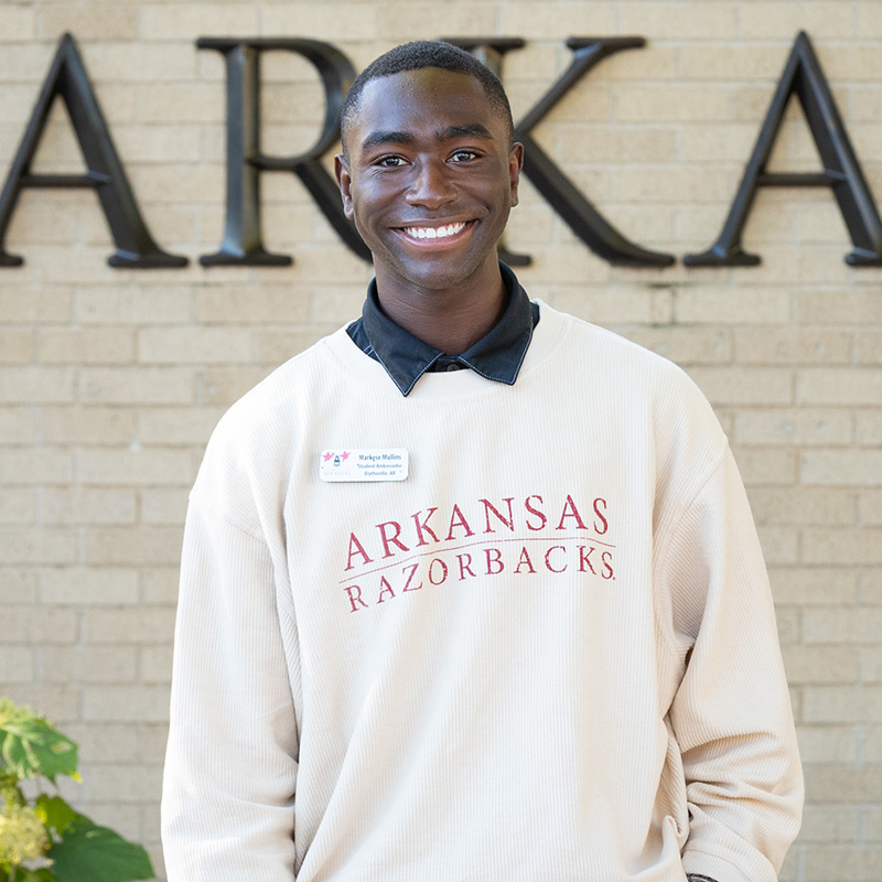 Markese Mullins stands in front of the University of Arkansas entrance sign